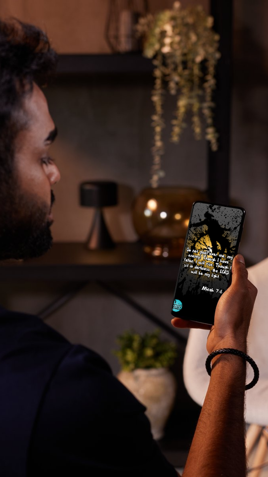 Person holding a phone with the stunning black and yellow design inspired by Micah 7:8 "Don't Gloat Over me" showing in a dimly lit room