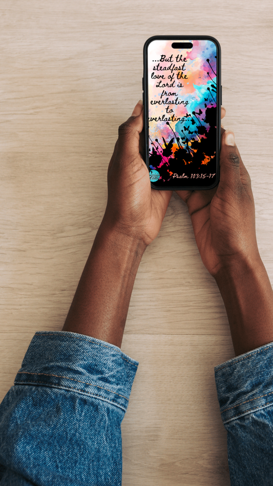 Person holding a phone with a colorful Bible verse lock screen on a wooden surface.
