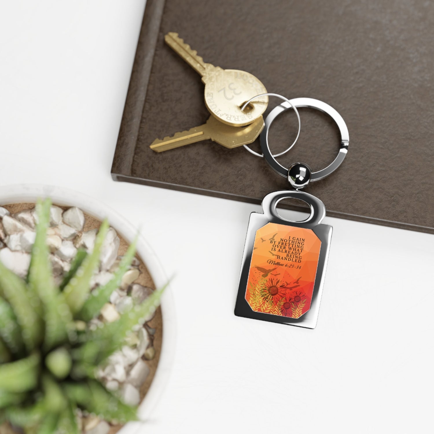 "I gain nothing by fretting" Christian Keychain from the Keys to Truth Christian Keychains example shot with keys sitting on a side table with a book and plant. 