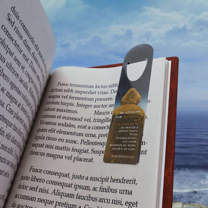 'Be Anxious for Nothing' -Philippians 4:6 Christian Bookmark Front view in use on example book page on the beach.