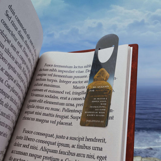 'Be Anxious for Nothing' -Philippians 4:6 Christian Bookmark Front view in use on example book page on the beach.
