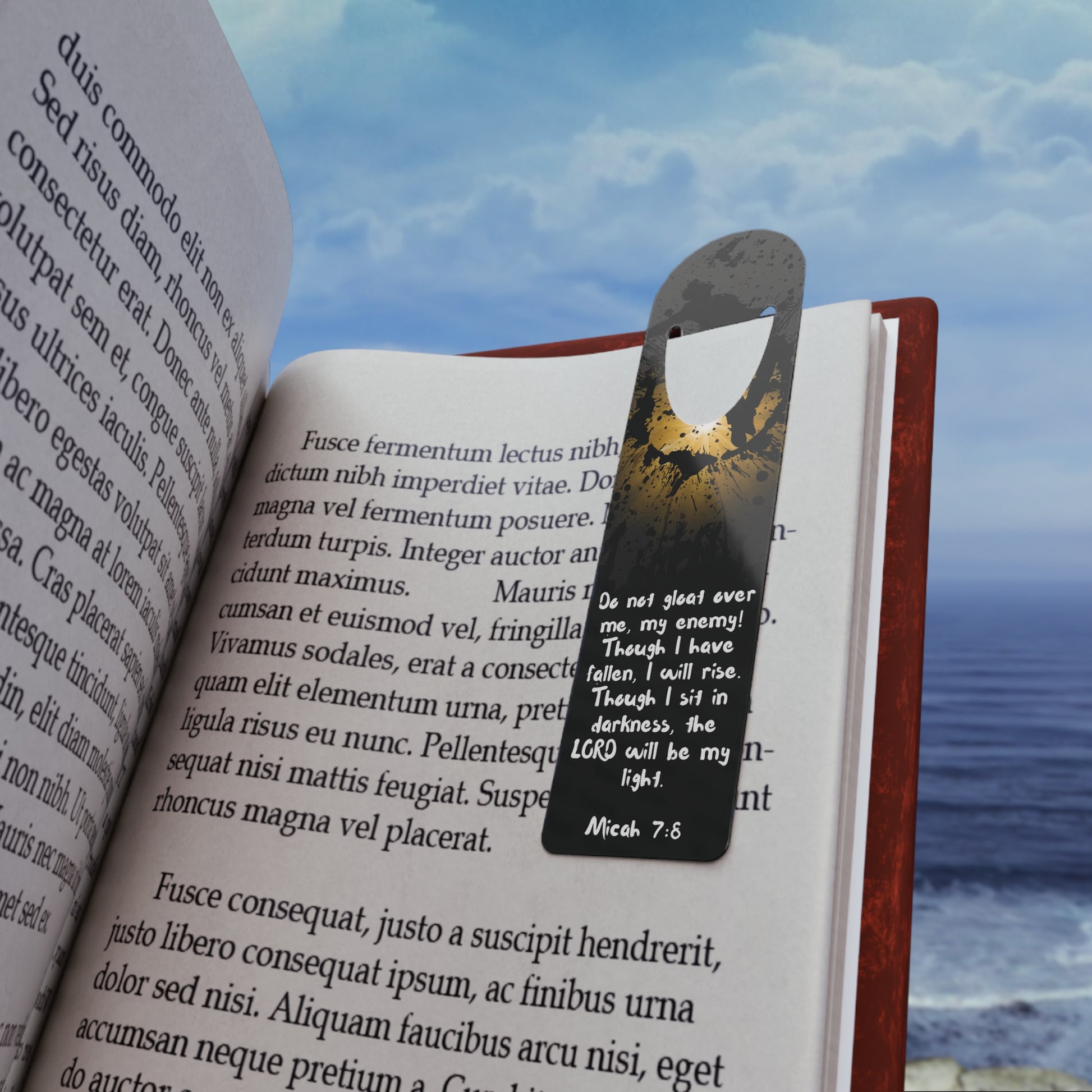 The Bible verse page marker "Don't Gloat over me", inspired by Micah 7:8, is clipped securely to a book page and held in front of a soft beach background. A Christian bookmark made for Bible study, devotionals, or gifting—mark the moment you didn’t quit trusting Him.