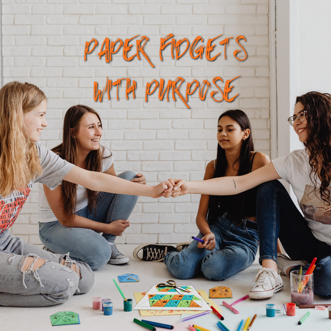 4 teenage girls sitting on the ground working on the Unfolding the Trinity flexagon project. Overlay text says: Paper Fidgets with Purpose.