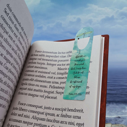'Uphold me according to Your Word' -Psalm 119:116 Christian Bookmark Front view in use on example book page on the beach.